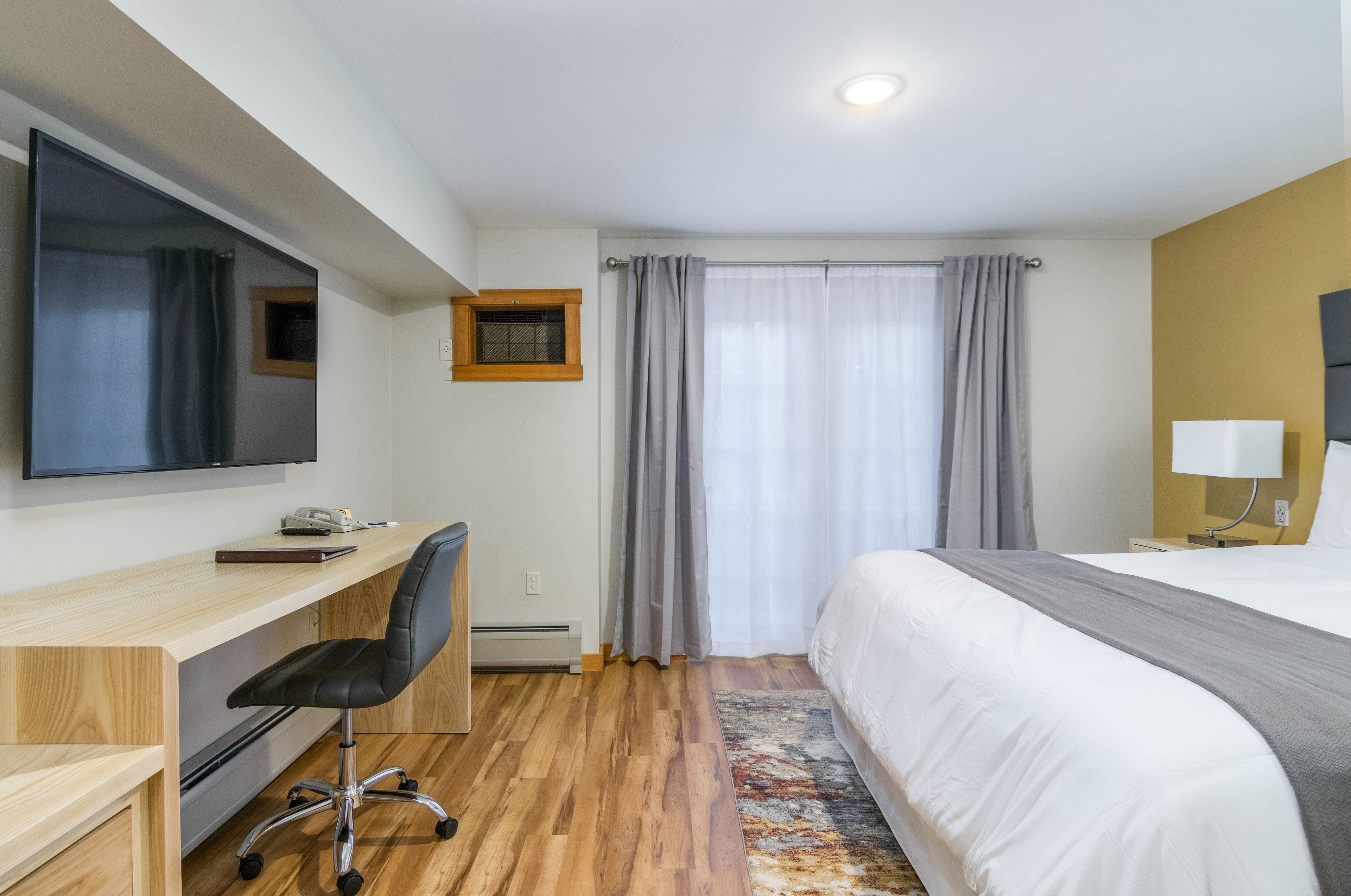 A hotel room with a bed, a desk with a chair, a television, and a window with curtains.