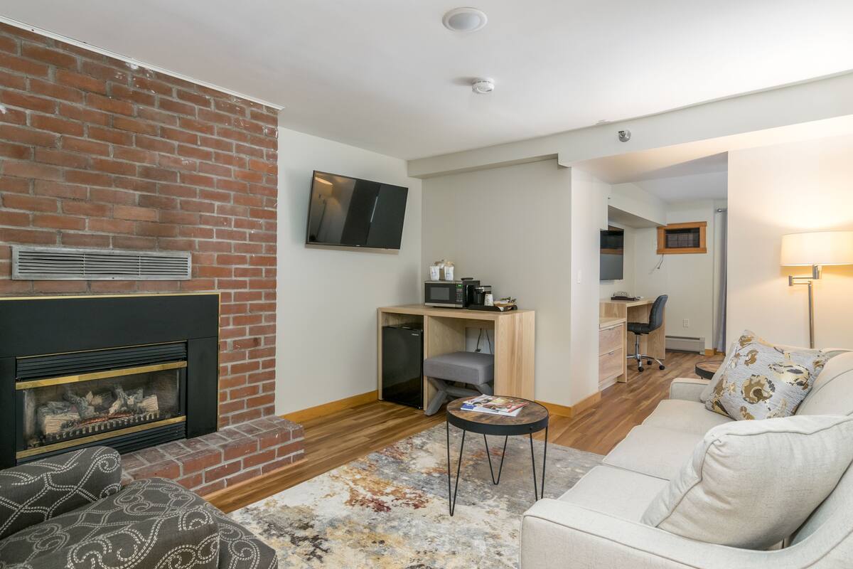 A living room with a fireplace, a television, a desk with a computer, and a sofa.