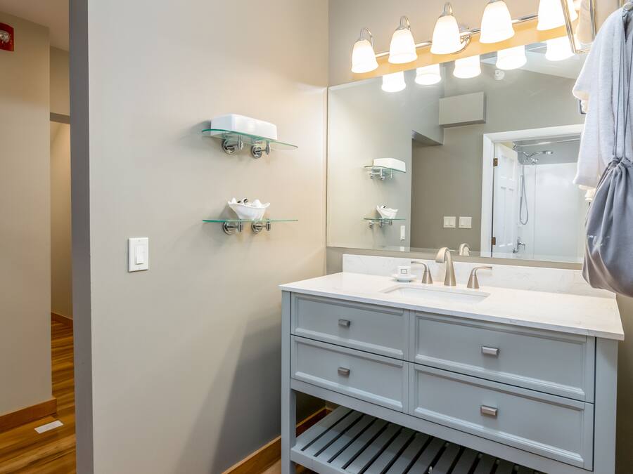 A modern bathroom with a white vanity, a large mirror, and three illuminated light fixtures above the mirror.