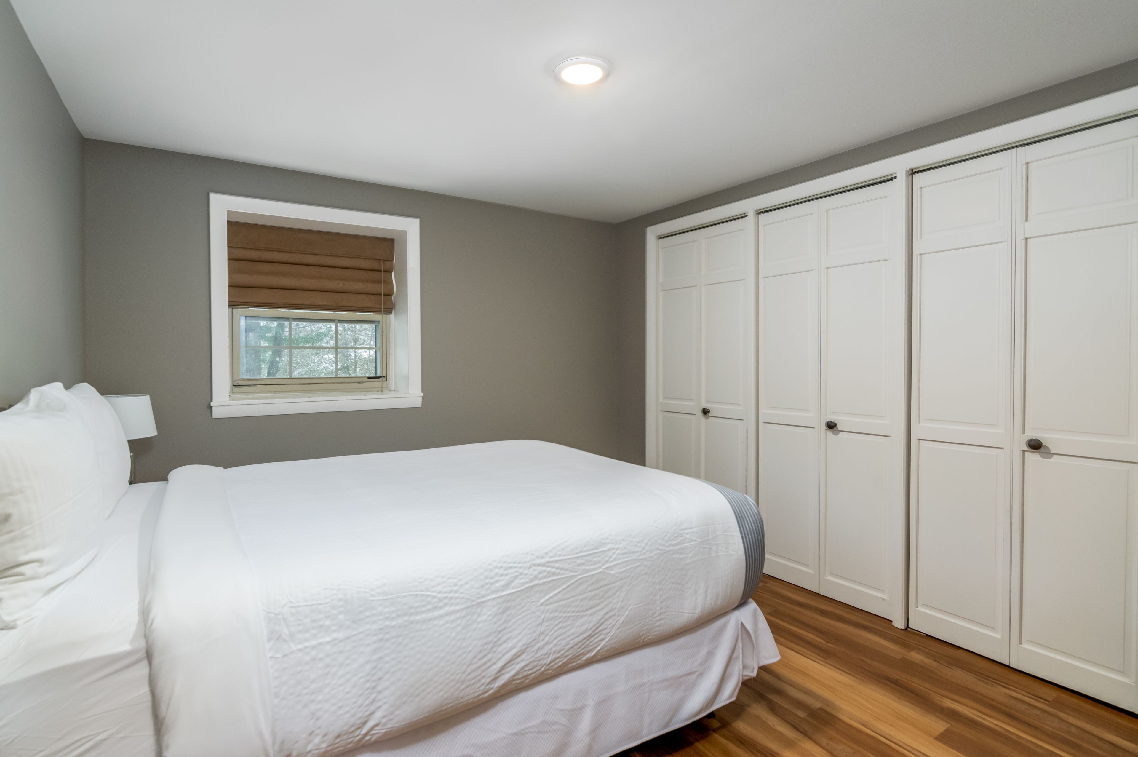 A bedroom with a bed, a window with blinds, a wardrobe, and a ceiling light.