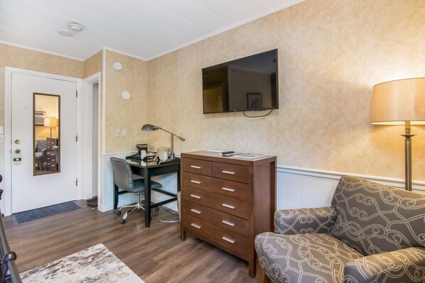 A room with a desk, chair, and a sofa. There is a TV mounted on the wall and a lamp on the floor.