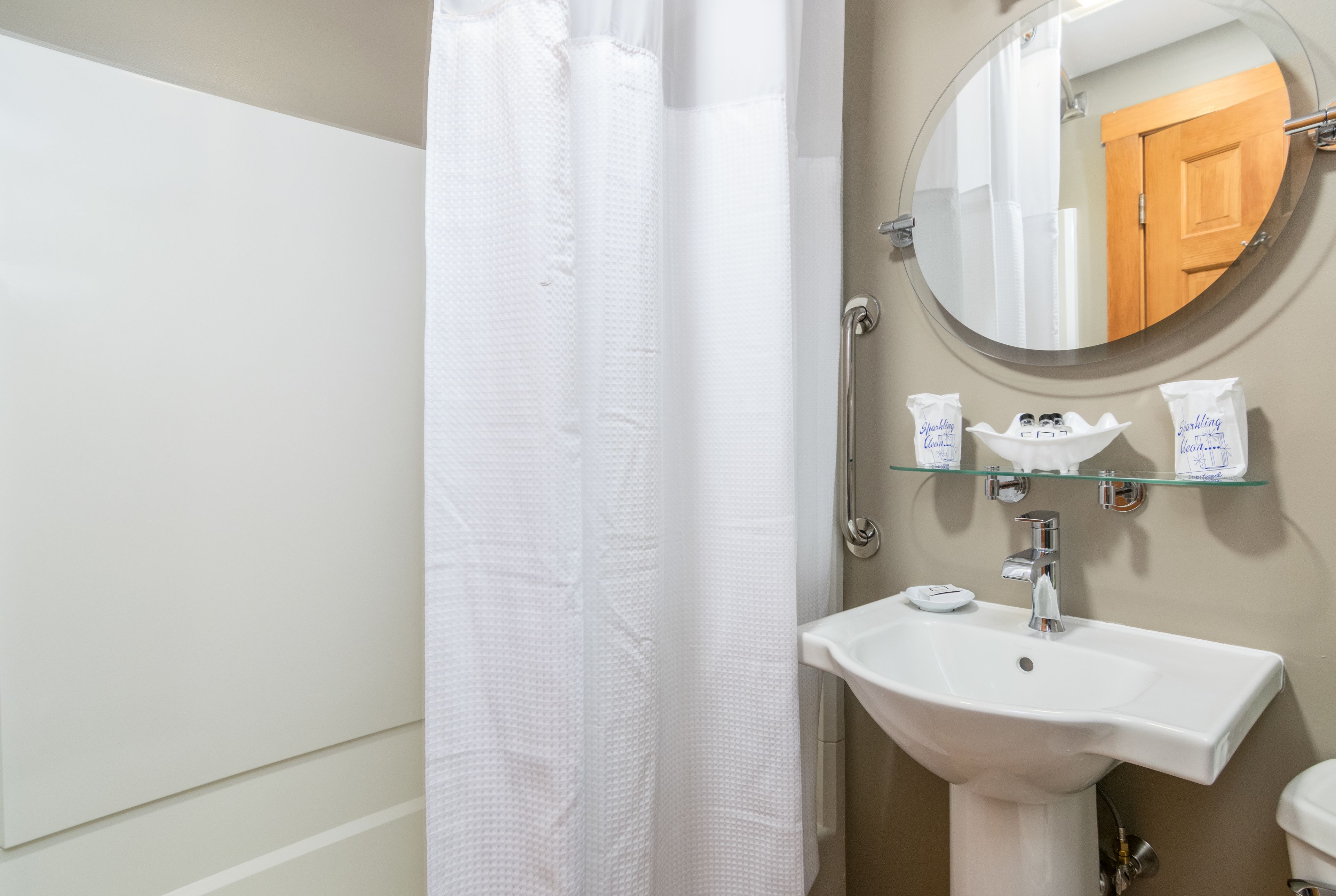 A bathroom with a white sink, a round mirror, and a shower curtain.