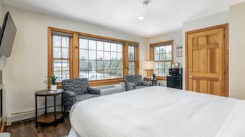 A bedroom with a large bed, two chairs, a small table, a TV, and a heater.