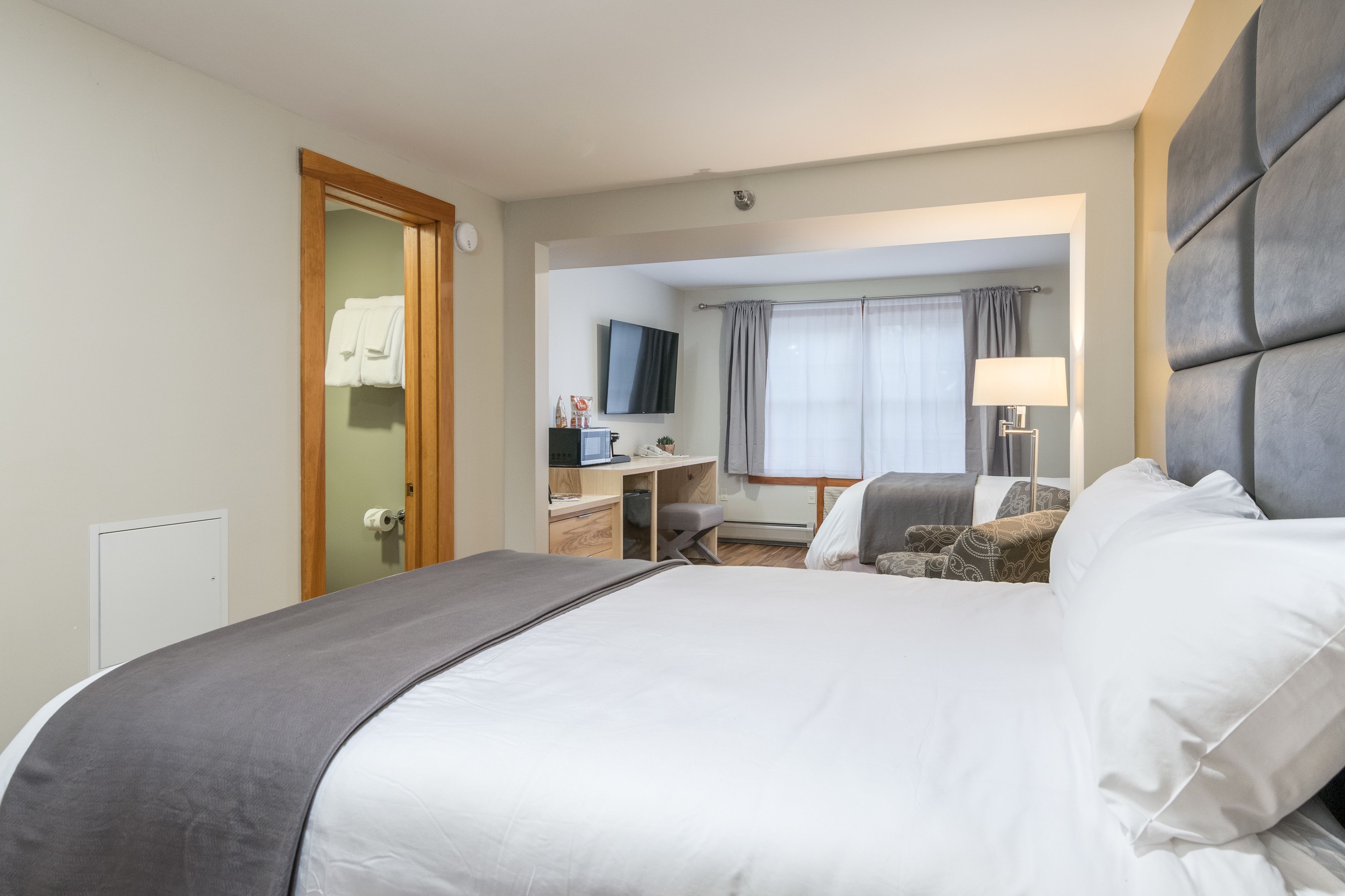 Ein Hotelzimmer mit einem großen Bett, einem Schreibtisch mit Computer, einem Fernseher und einem Fenster mit Vorhängen.