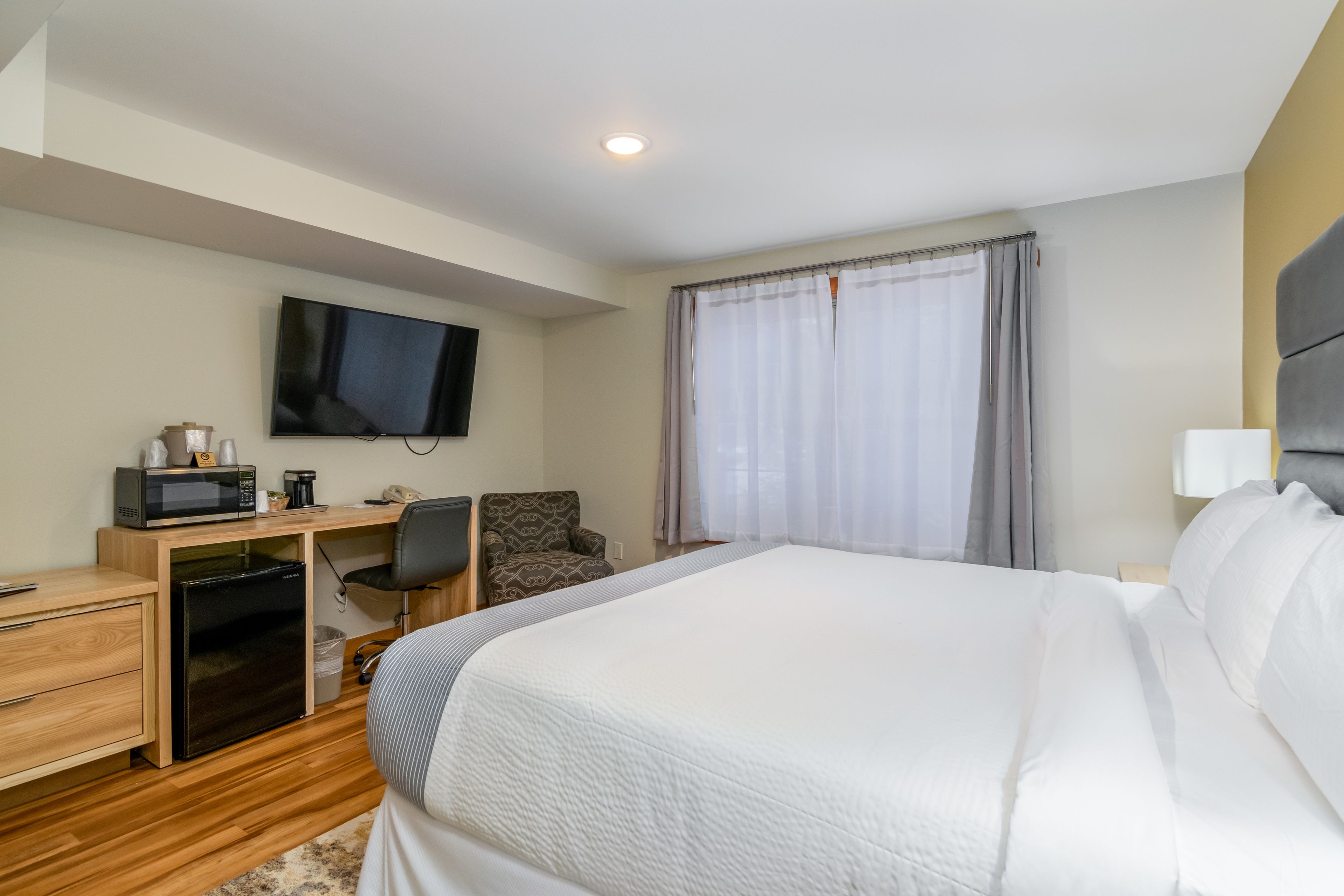 Una habitación de hotel con cama, escritorio con computadora, televisión y ventana con cortinas.