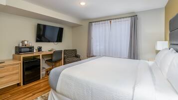 Una habitación de hotel con cama, escritorio con computadora, televisión y ventana con cortinas.