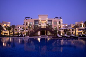 A hotel with a central staircase, a swimming pool, and multiple lounge areas. - Shangri-La Hotel Apartments Qaryat Al Beri (Abu Dhabi)