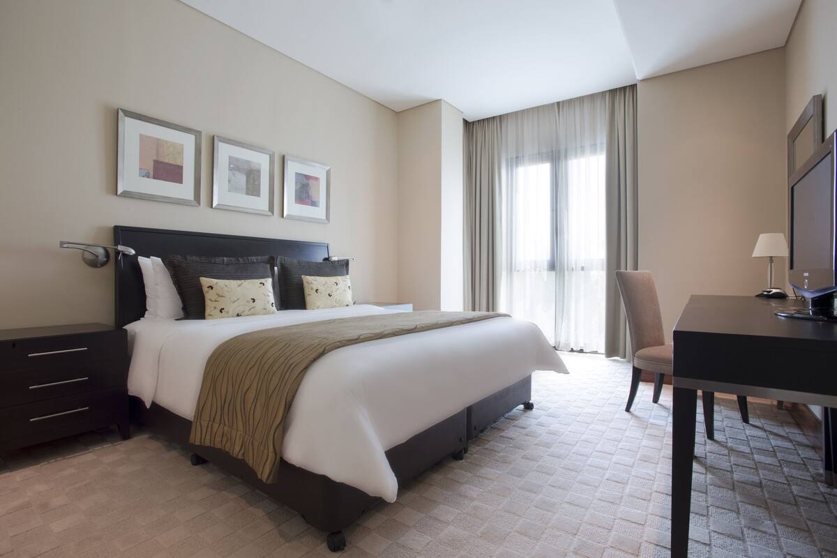 A hotel room with a large bed, bedside tables, a desk, and a chair. There are three framed pictures on the wall.