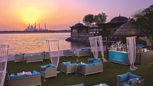 Terraza con asientos al aire libre, un bar y vistas a una mezquita y al atardecer sobre el agua.