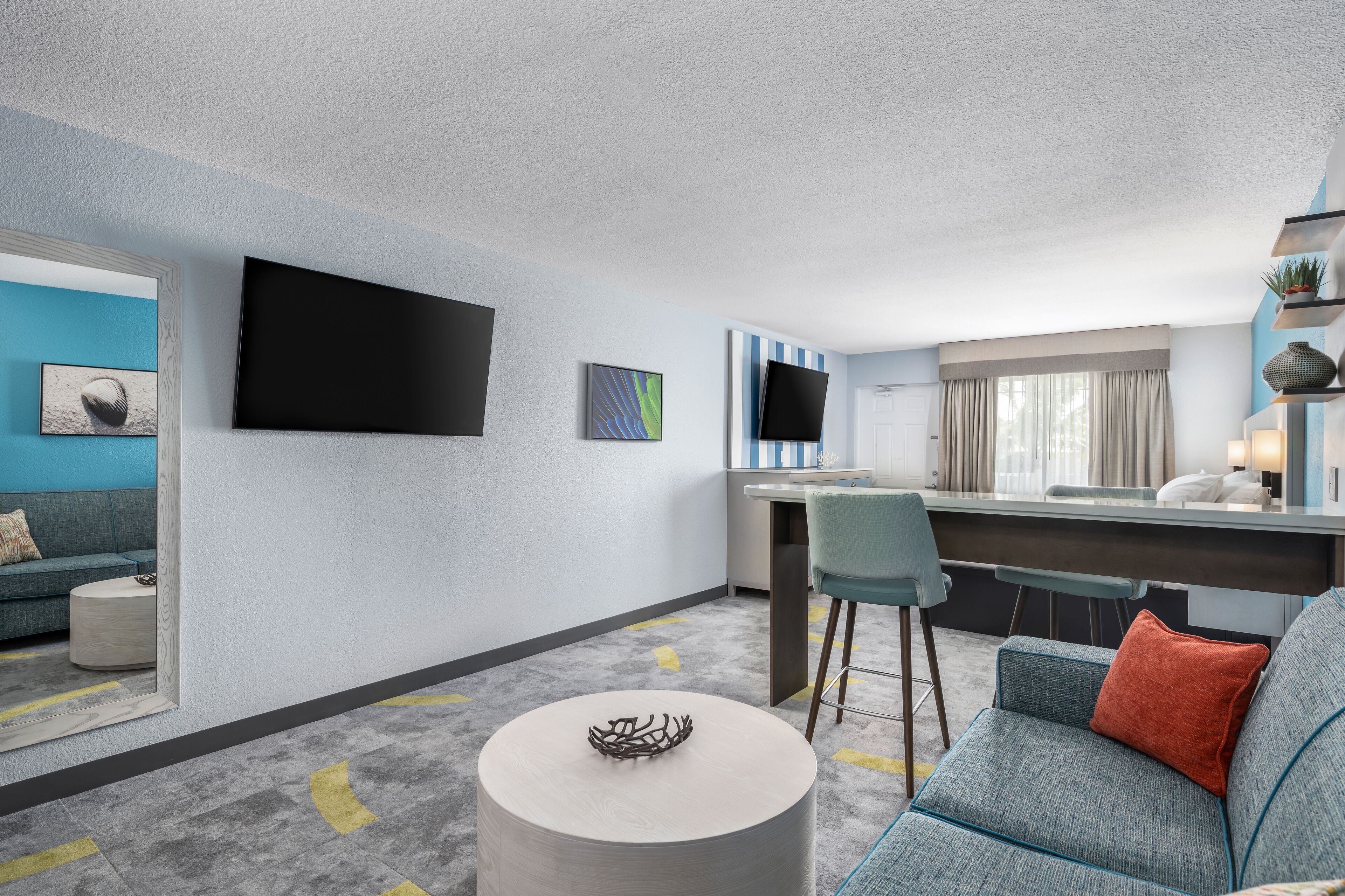 Een moderne hotelkamer met een zithoek, een eethoek, een flatscreen televisie en een klein barretje.
