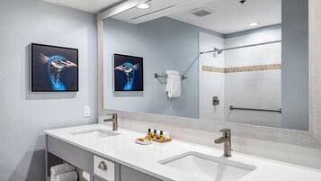Une salle de bain moderne avec deux lavabos, un grand miroir et des œuvres d’art accrochées au mur.