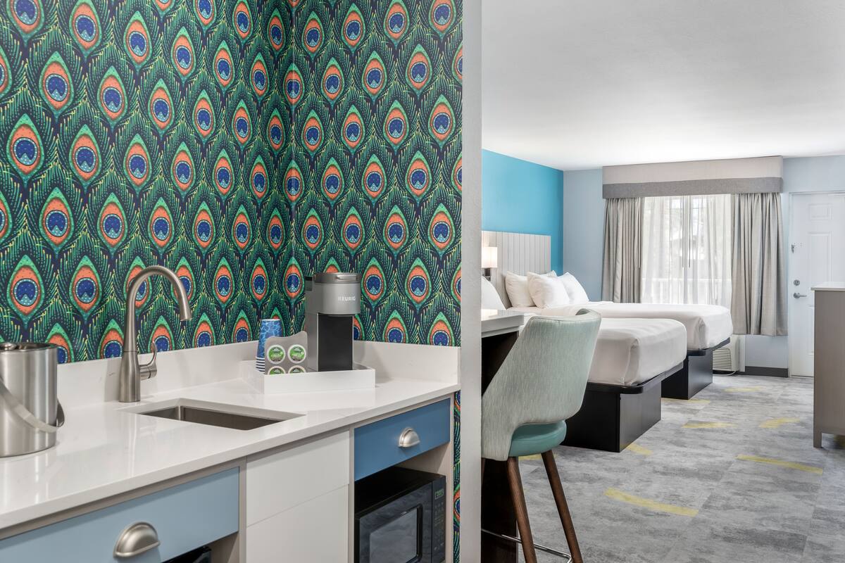 A hotel room with a kitchenette, a bed, a desk, and a bathroom.