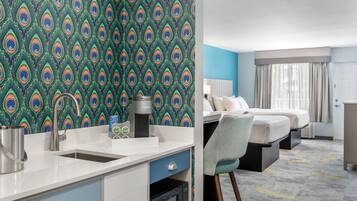 A hotel room with a kitchenette, a bed, a desk, and a bathroom.