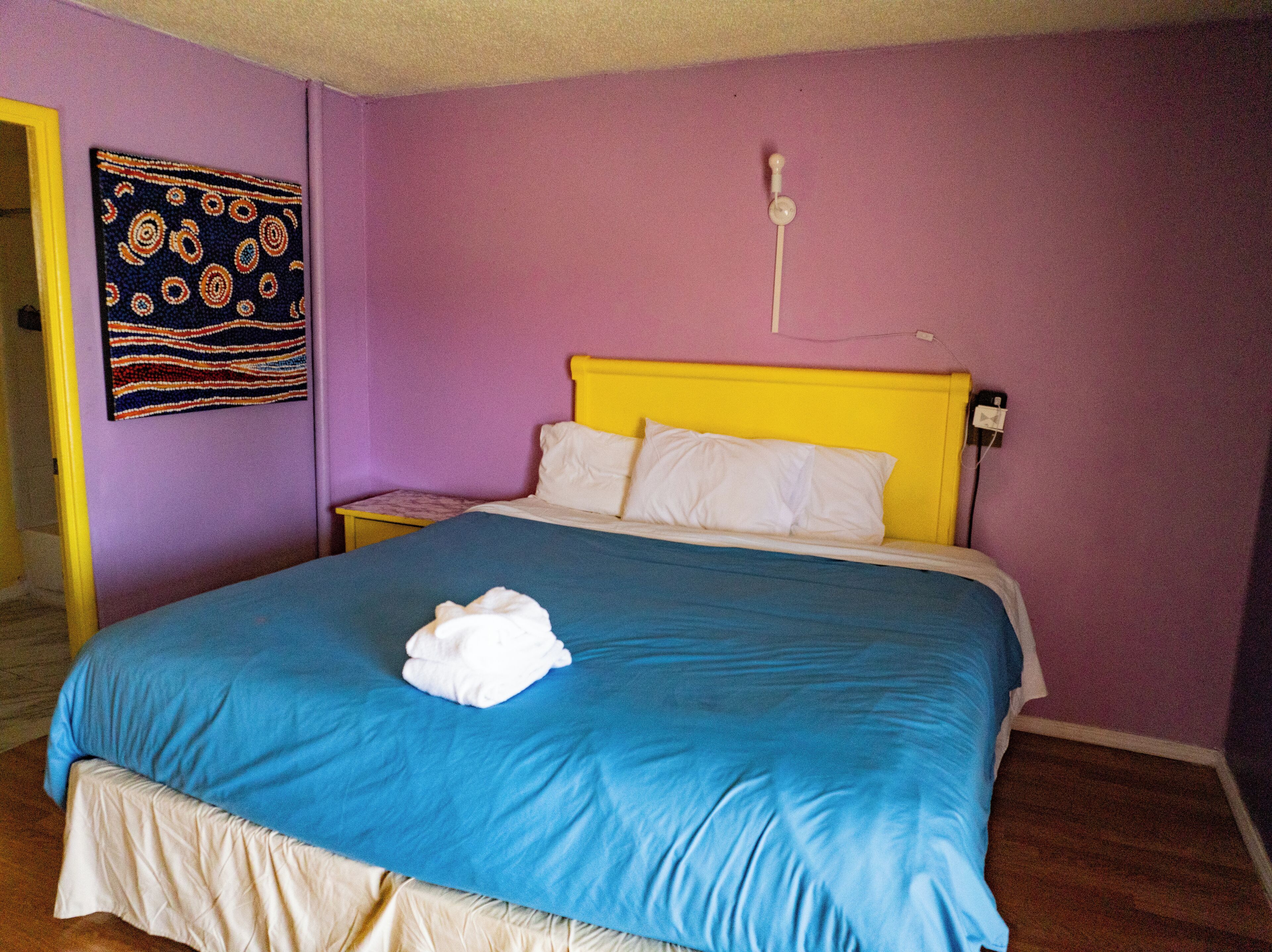 Cama con cubrecama azul, almohadas blancas y cabecero amarillo, además de un enchufe en la pared.