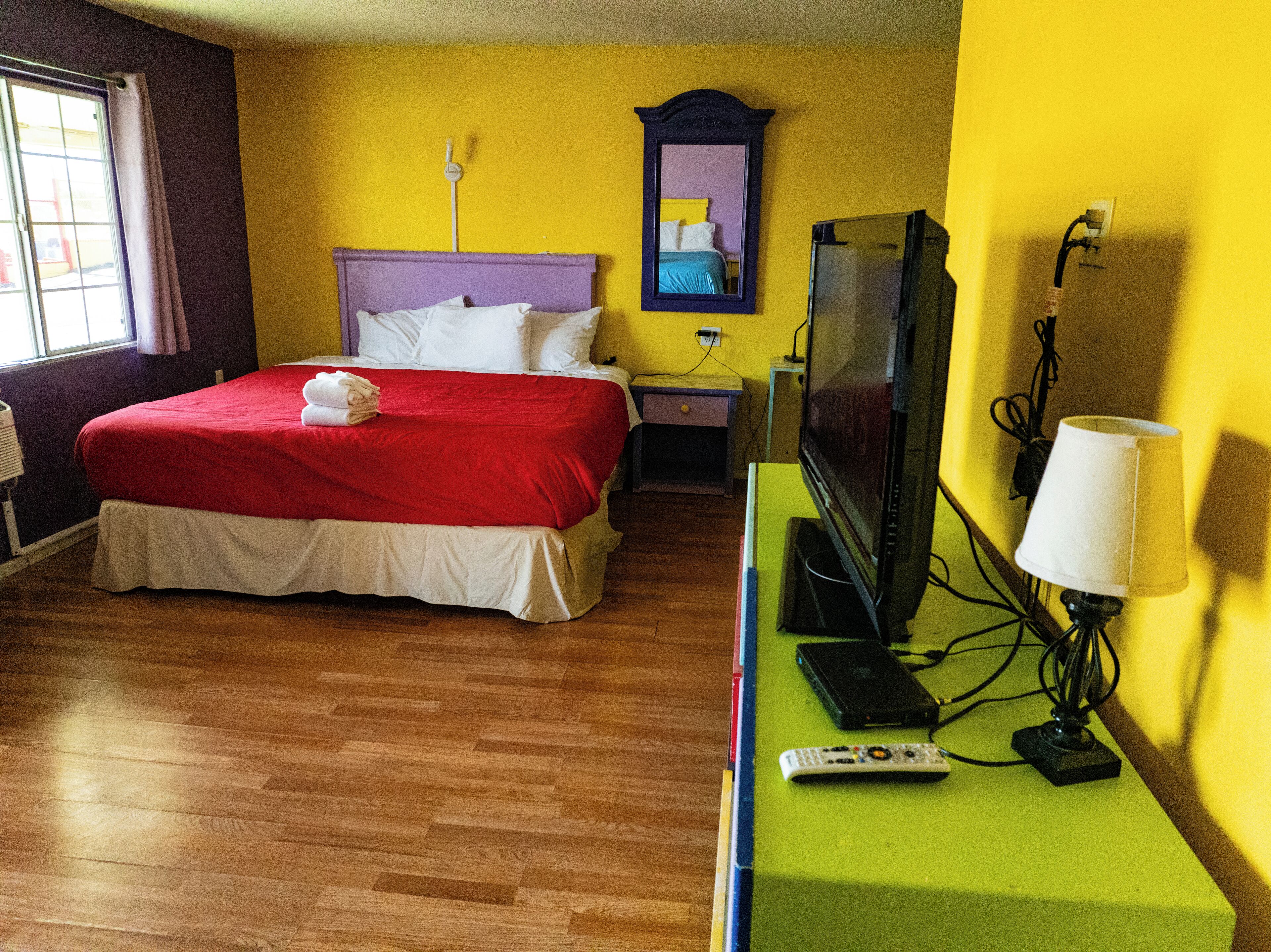 A hotel room with a bed, a television, a lamp, and a remote control on a green table.
