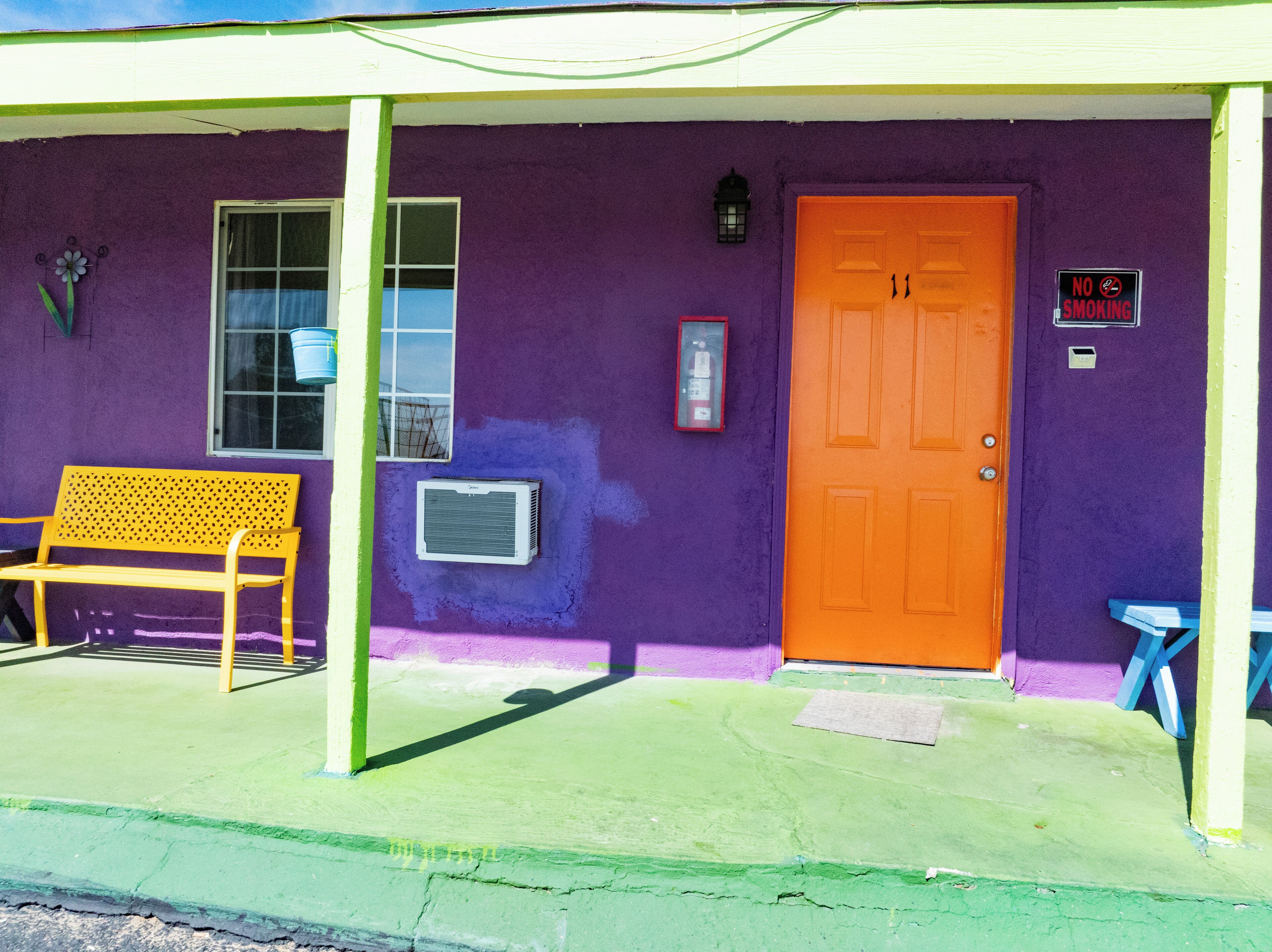 Un edificio con fachada morada, una banca de madera, una puerta y un letrero que indica que no se permite fumar.