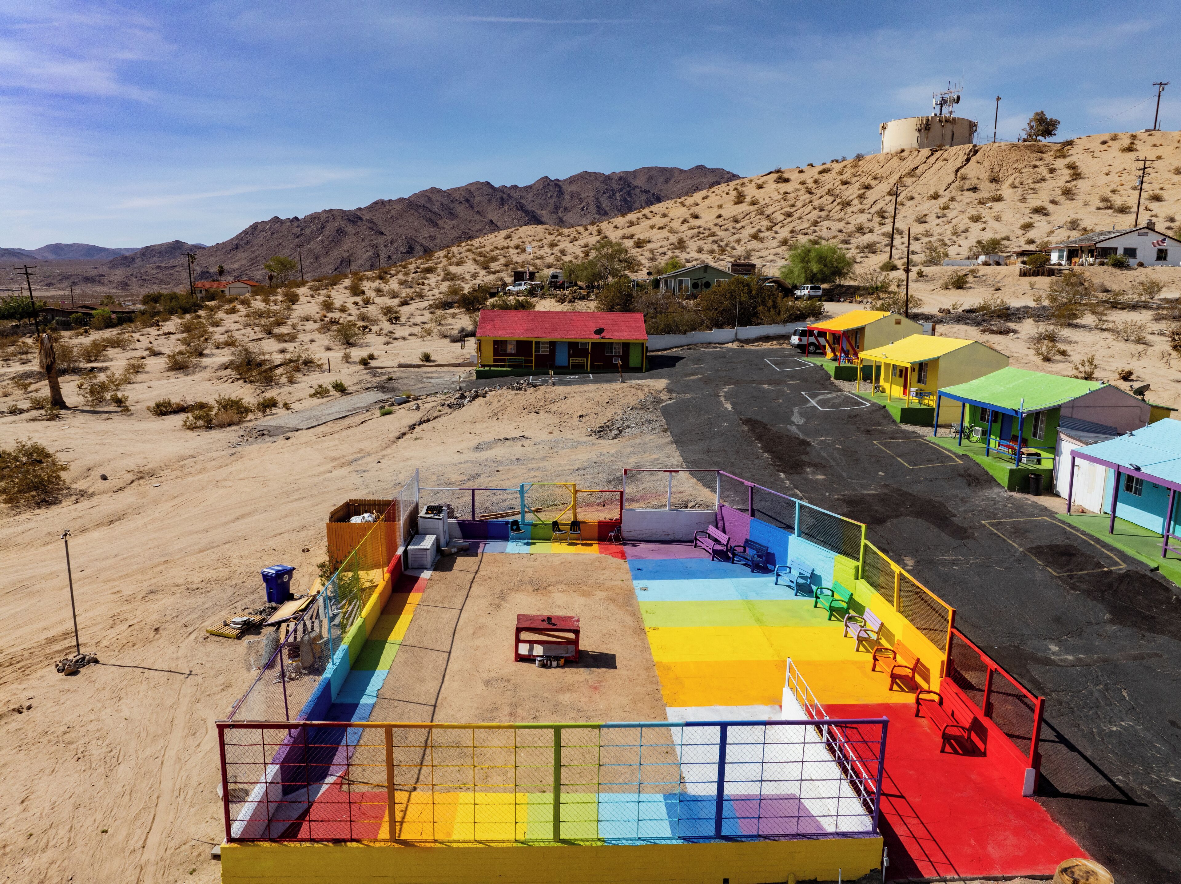 Une aire de jeux colorée, délimitée par une clôture, avec un petit bâtiment doté d’un toit rouge et un chemin menant à une colline à la végétation clairsemée.