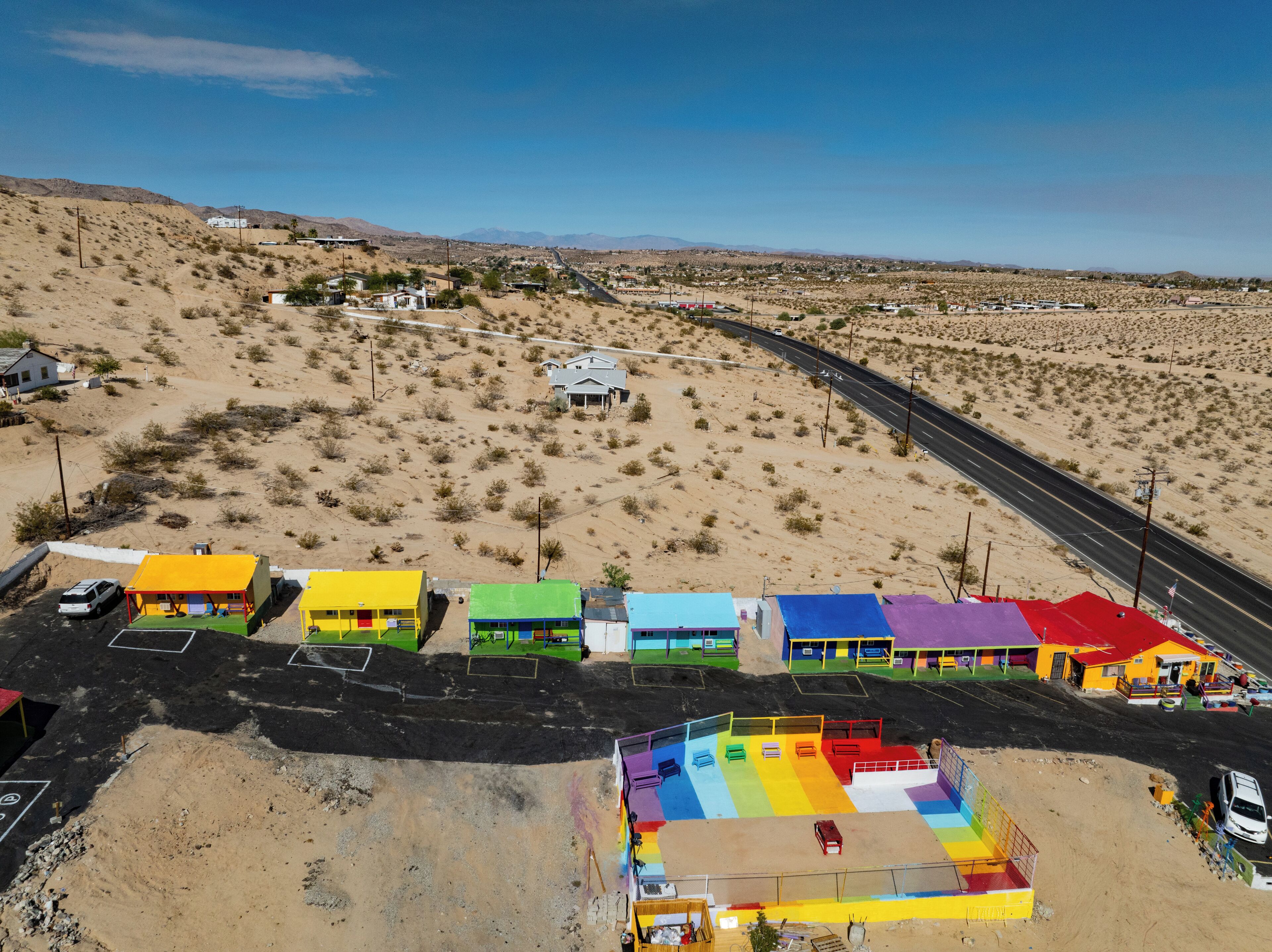 Paisaje desértico con una carretera serpenteando a través de él. Hay edificios coloridos a lo largo de la carretera, algunos de varios pisos.