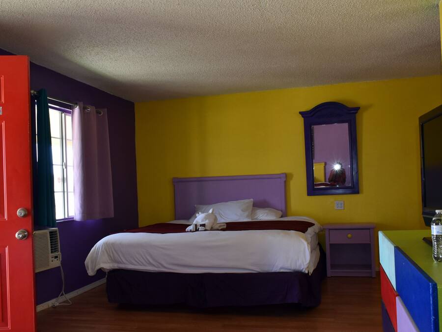 Een kamer met een bed, een televisie, een waterfles en een rode deur met een 'Niet roken'-bord.