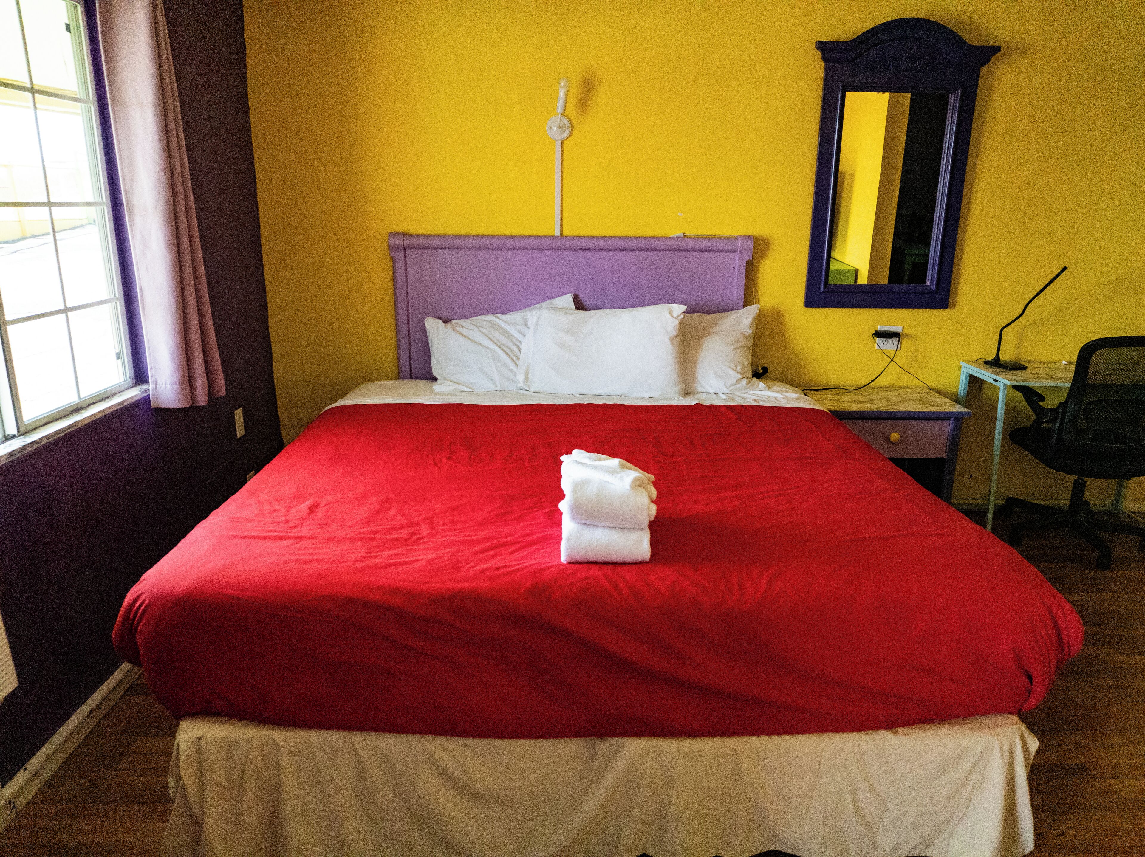 A hotel room with a bed, a desk, a chair, and a mirror.