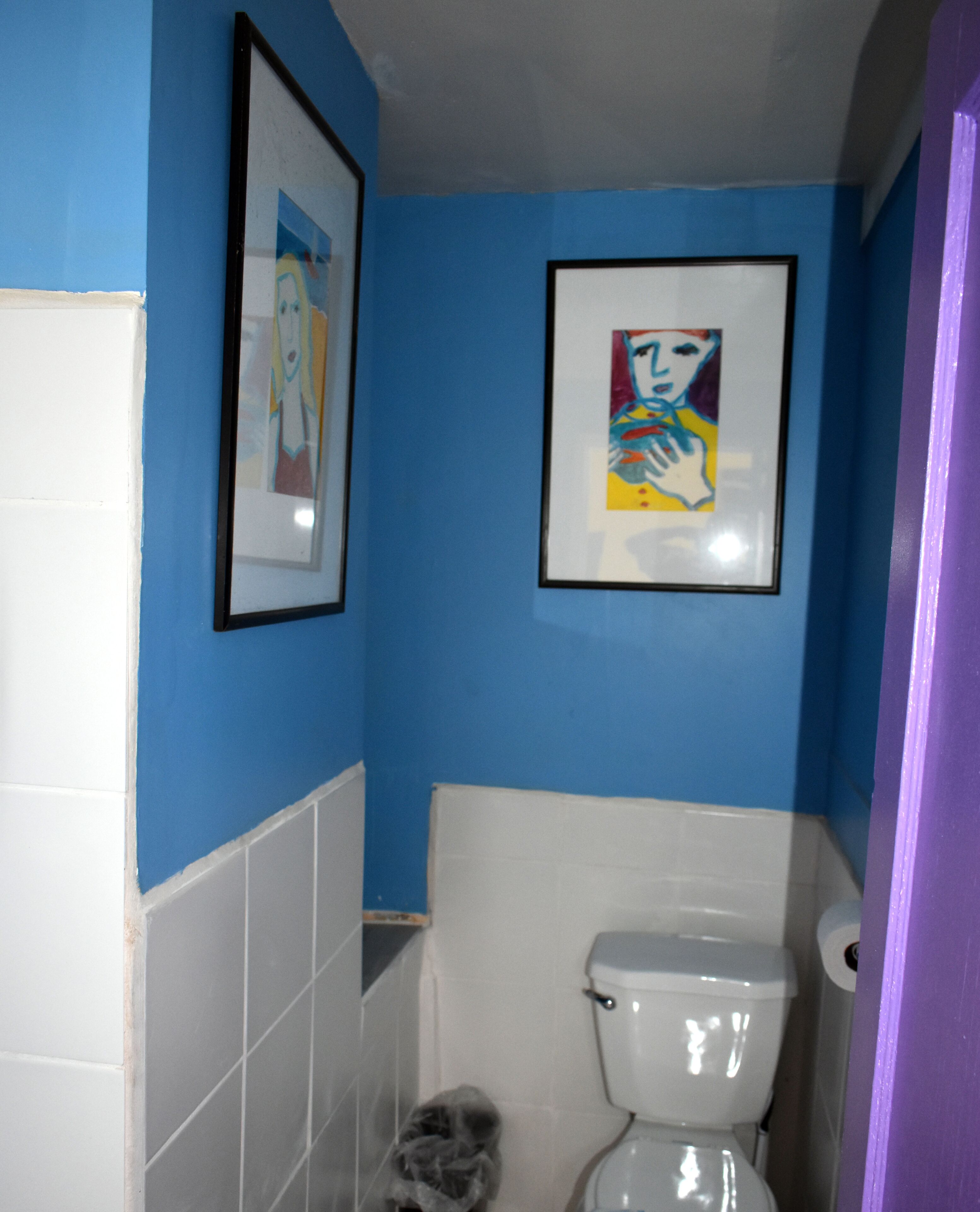 Un baño con paredes azules, un inodoro blanco y dos cuadros en la pared.