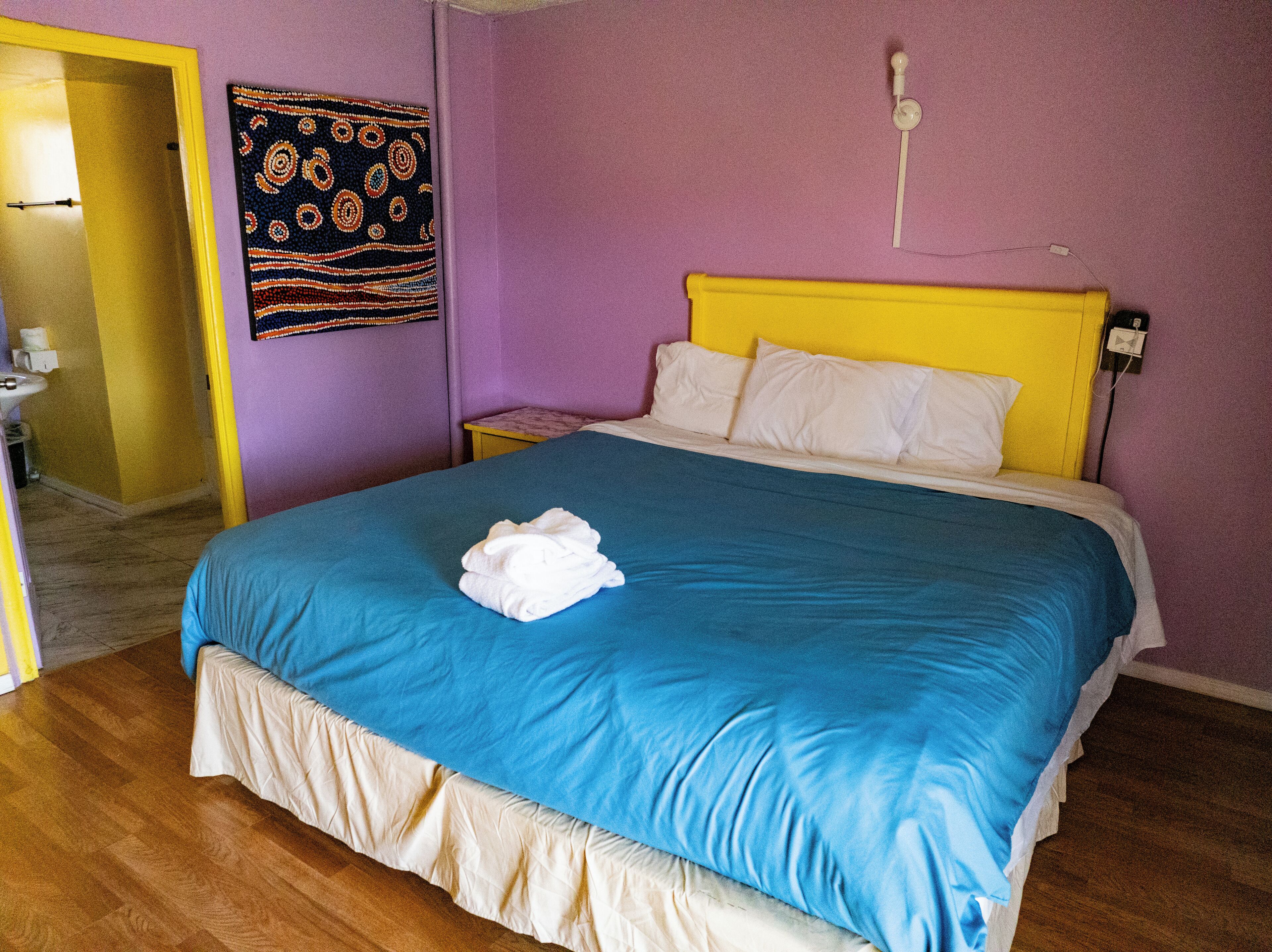 Een kamer met een bed, een nachtkastje, een wandlamp en een deur naar een andere kamer.