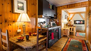 Un interior rústico de madera con una mesa de comedor, sillas, una zona de cocina y un espacio de sala acogedor.