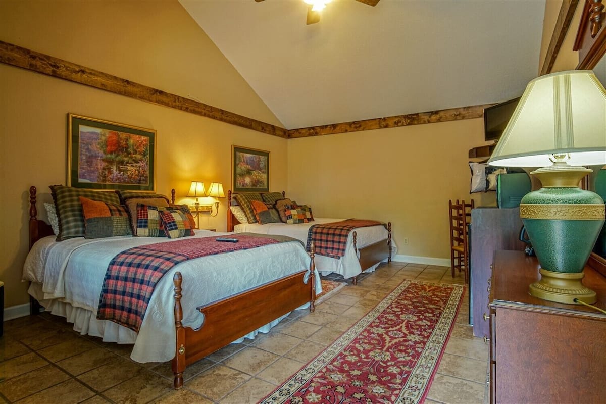 A bedroom with two beds, a wooden headboard, a red and white patterned rug, and a green lamp.