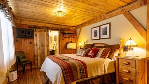Un dormitorio acogedor con techo de madera, una cama con muchas almohadas, una mesita de noche con lámpara y una silla.