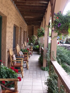 A covered outdoor seating area with wooden chairs and tables, surrounded by potted plants and flowers.