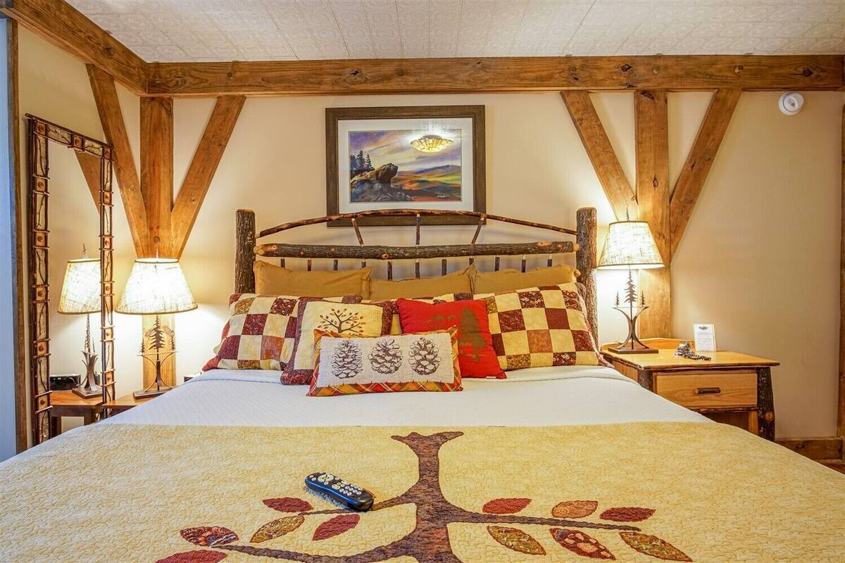 A cozy bedroom with a wooden bed frame, a large bedspread with a tree design, and two bedside lamps.