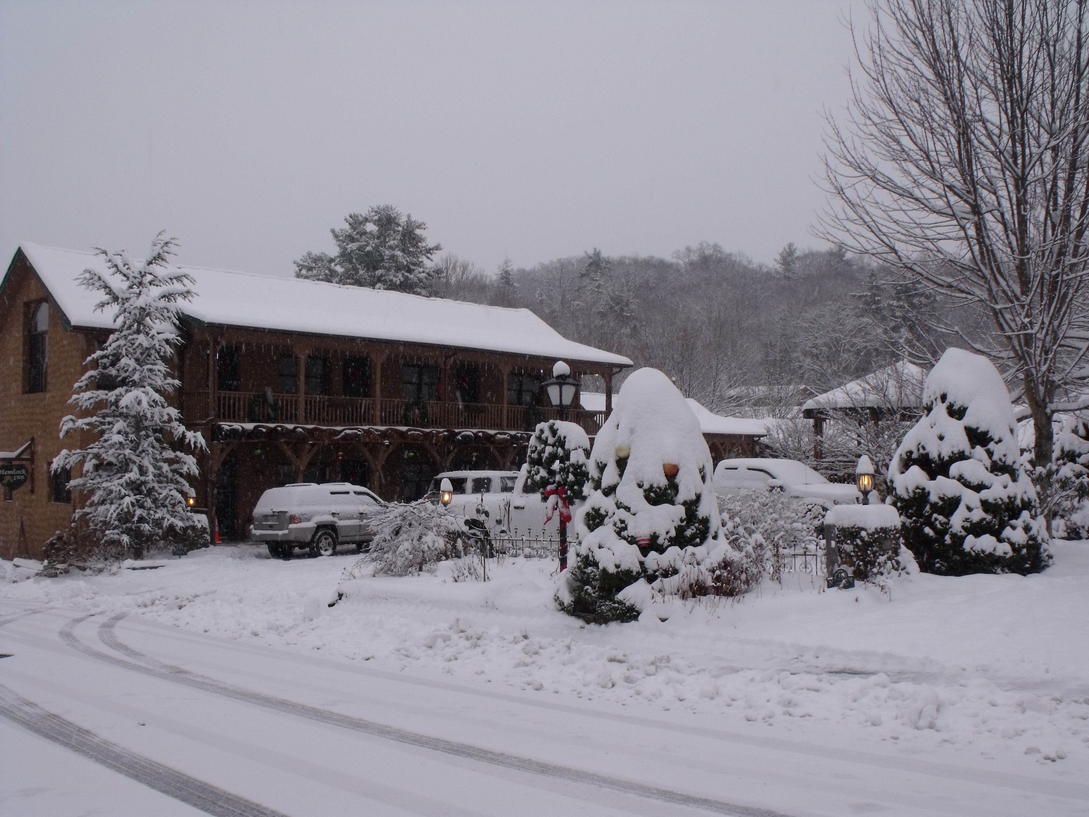 Een gebouw bedekt met sneeuw, met een houten gevel, een overdekte oprit en sneeuwzware bomen.