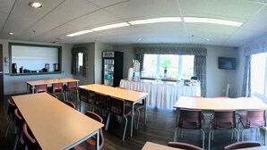 A dining area with tables and chairs, a counter with food items, and a television on the wall. - Glendenning Hall (Charlottetown)