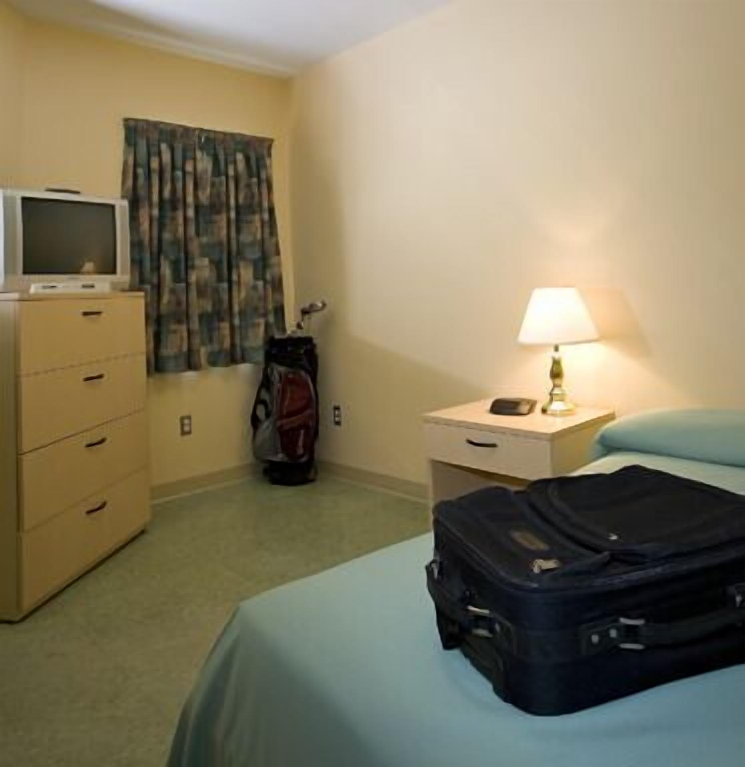 Una camera d'albergo con un letto, una cassettiera, un televisore, una lampada e una valigia.