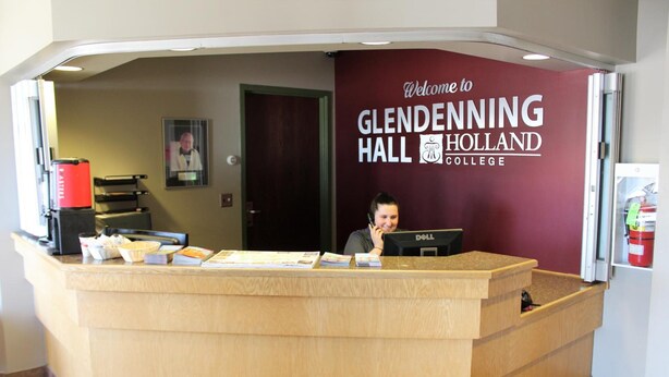 A reception desk at Glendenning Hall Holland College with a red wall, a framed picture, and a Dell computer. - Glendenning Hall (Charlottetown)