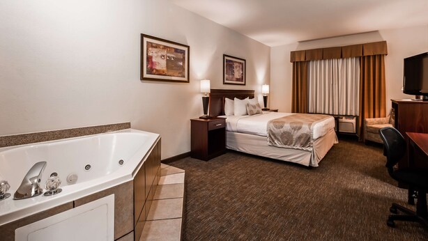 A hotel room with a large bathtub, a bed with a headboard, a desk with a chair, and two bedside lamps. - Best Western Jacksonville Inn (Jacksonville)