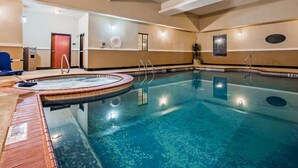 A large indoor swimming pool with clear water, a hot tub, and a lounge area with a blue chair. - Best Western Jacksonville Inn (Jacksonville)