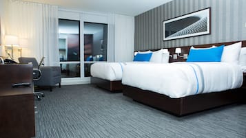 A hotel room with two beds, a desk, a chair, and a large window with curtains.