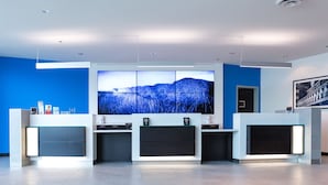 A modern reception area with a blue wall, a large landscape painting, and a reception desk with a flat-screen TV. - The Grand Winnipeg Airport Hotel by Lakeview (Winnipeg)