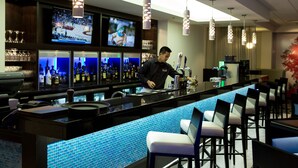A bar area with a counter, bar stools, and a television displaying a sports event. - The Grand Winnipeg Airport Hotel by Lakeview (Winnipeg)