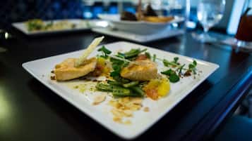 A dining table with a white plate containing a fish dish, green beans, and garnishes.