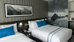 A hotel room with two beds, a nightstand with a phone and lamp, and a large wall mural of mountains and a stormy sky. - The Grand Winnipeg Airport Hotel by Lakeview (Winnipeg)