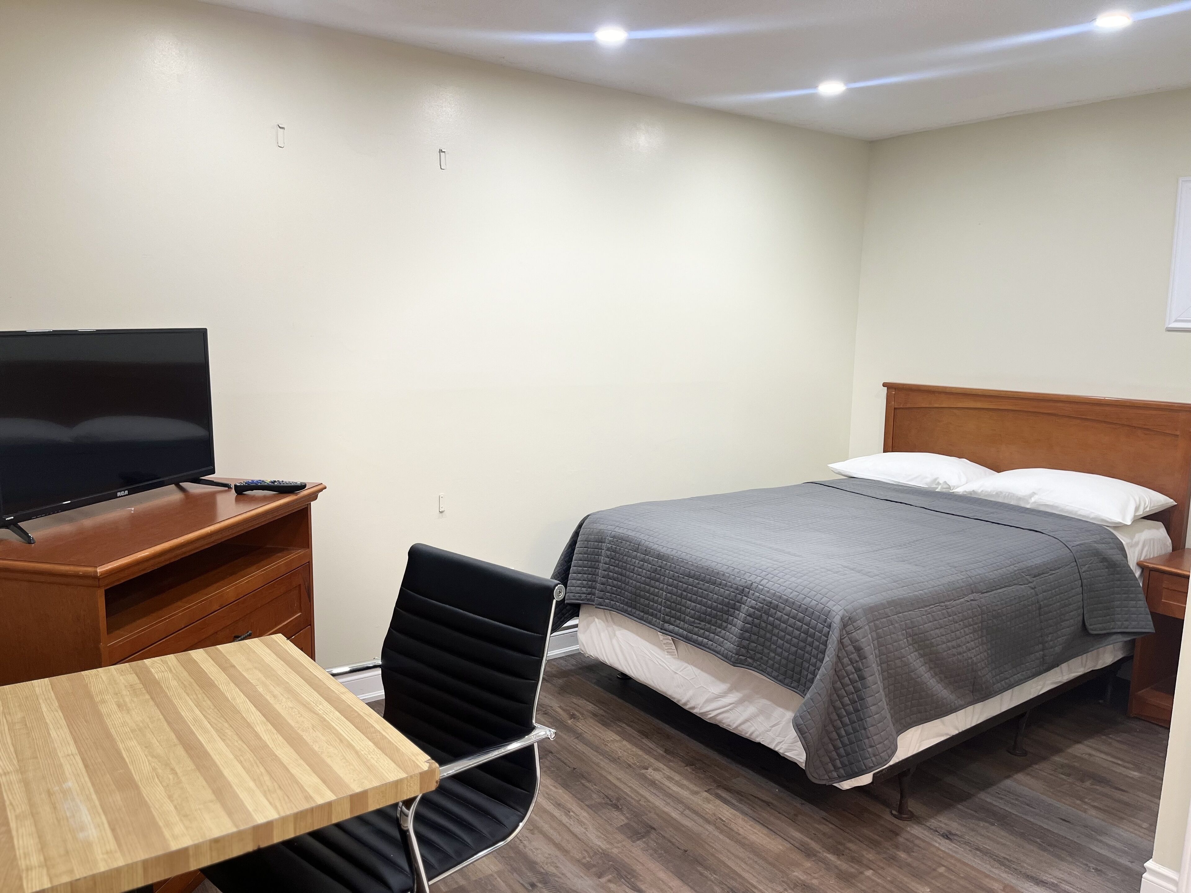 A hotel room with a bed, a TV on a wooden table, a chair, and a wooden nightstand.