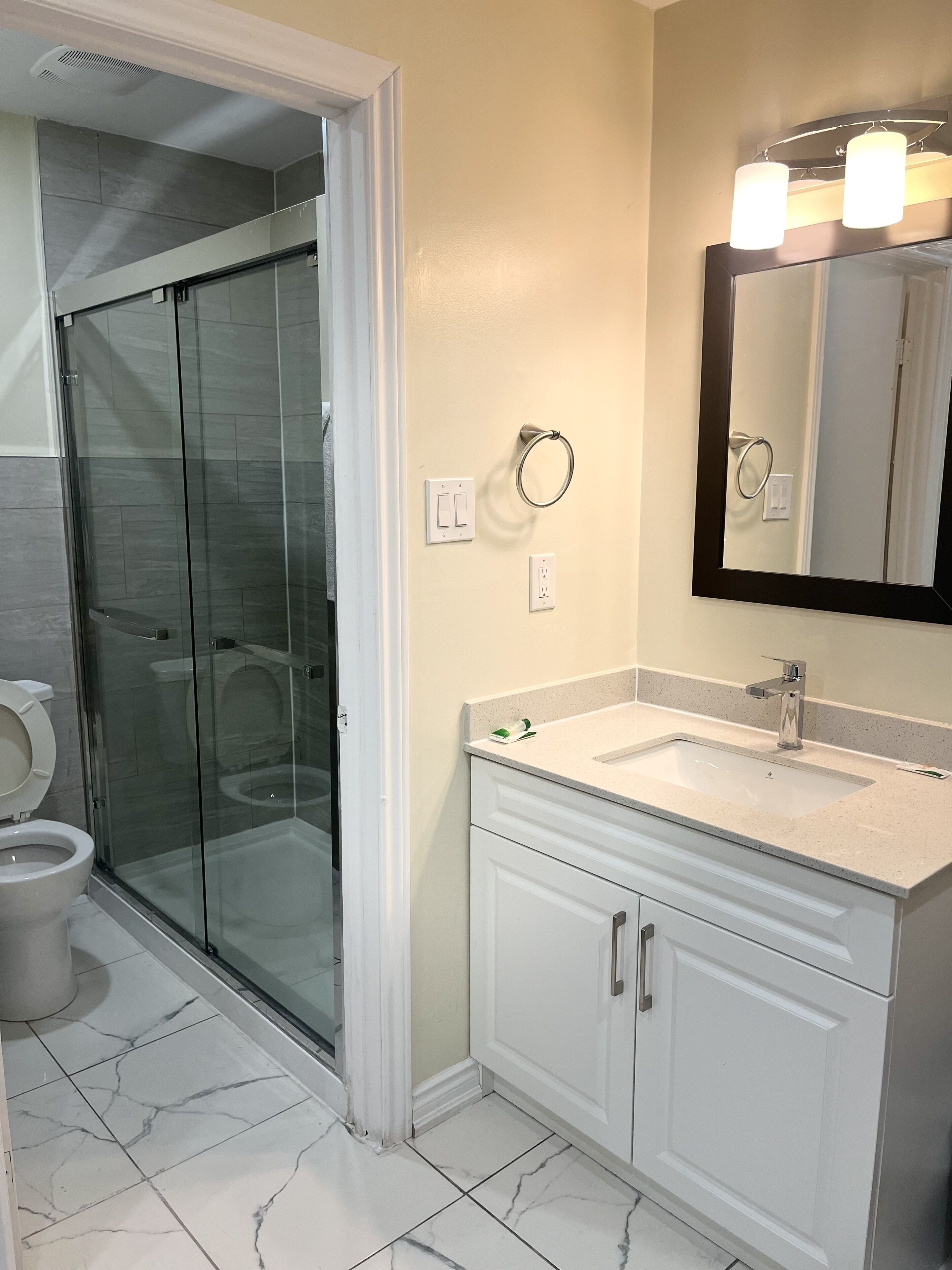 A bathroom with a glass shower enclosure, a toilet, a sink with a mirror, and a towel ring.