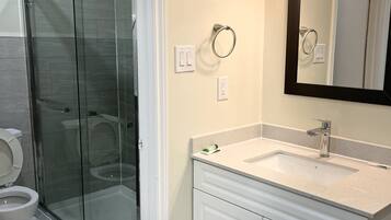 Een badkamer met een douchecabine van glas, een toilet, een wastafel met spiegel, en een handdoekhouder.