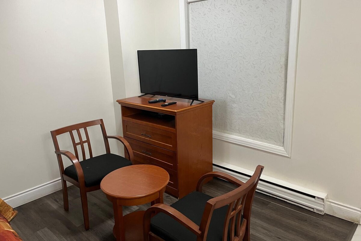 A small room with a desk, two chairs, a television, and a window.