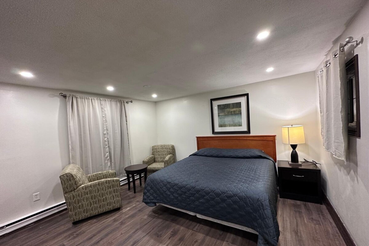 A hotel room with a bed, a chair, a small table, a lamp, and a picture on the wall.
