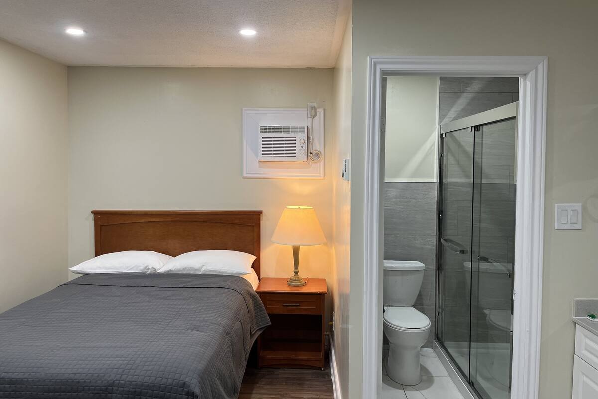 Une chambre à coucher avec un lit, une lampe de chevet, et une salle de bain avec des toilettes et une douche.