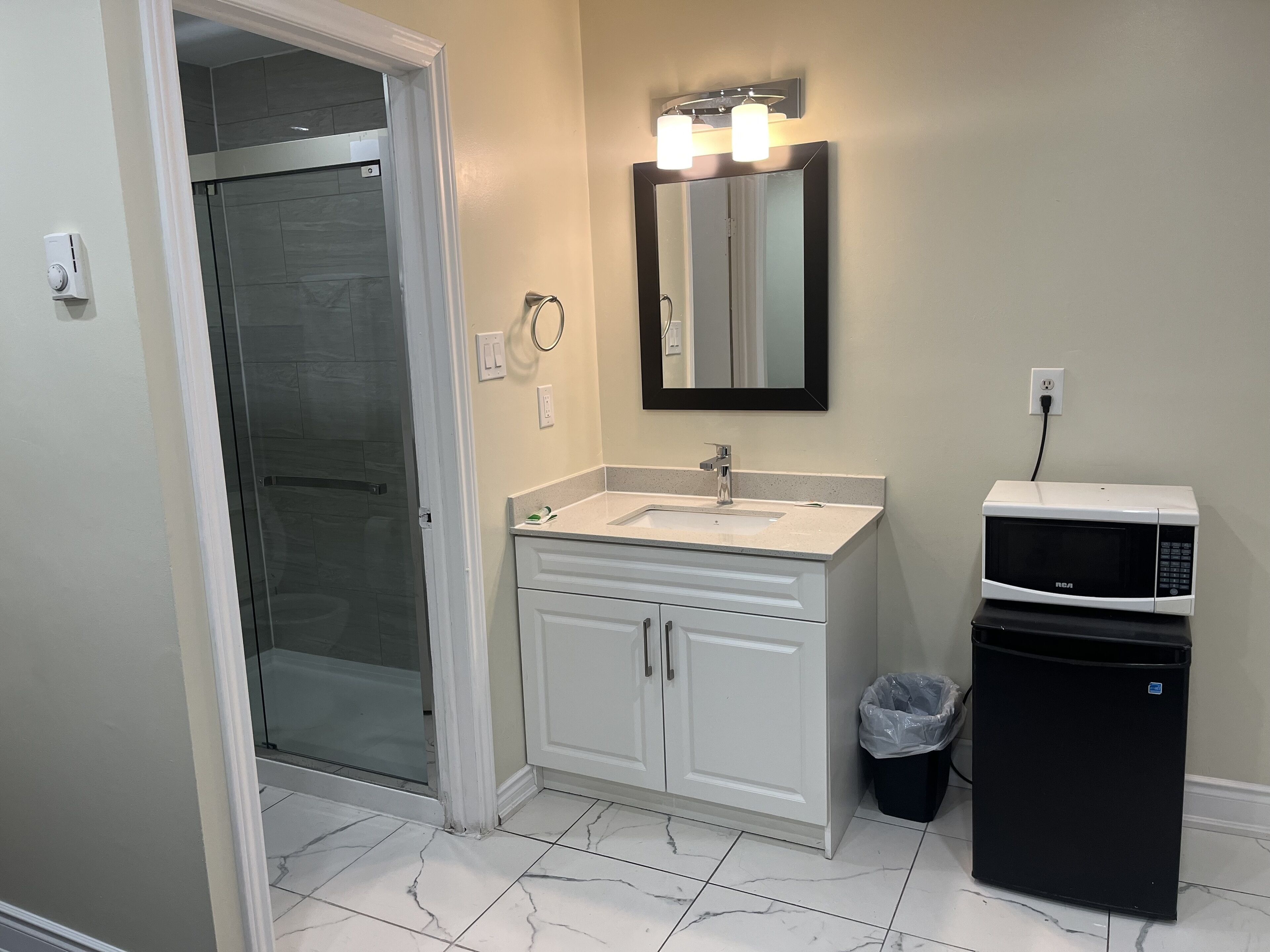 Un baño con mampara de vidrio, lavabo con espejo arriba y microondas sobre la encimera.