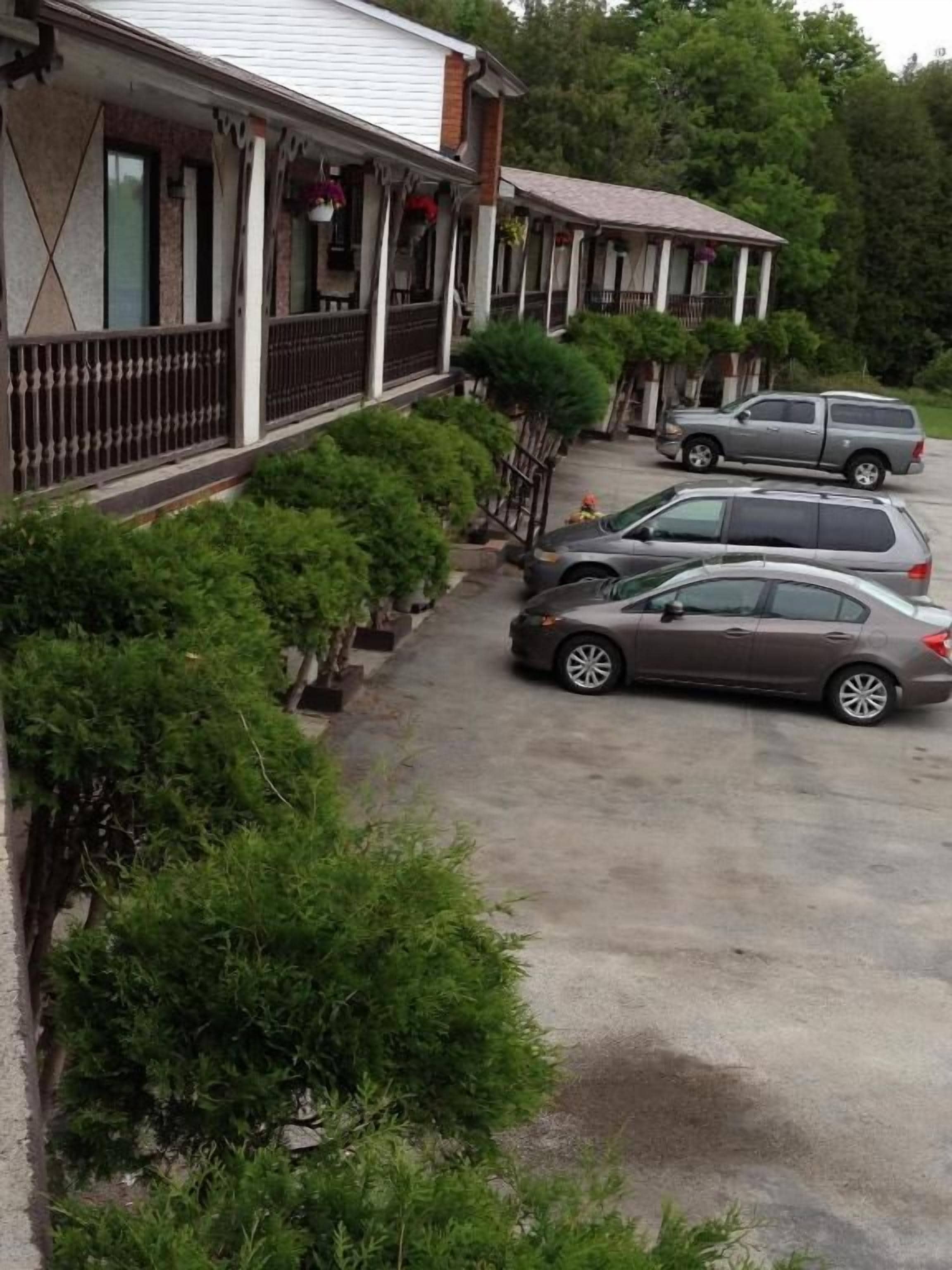 A row of two-story buildings with a covered porch and a parking area with two cars.